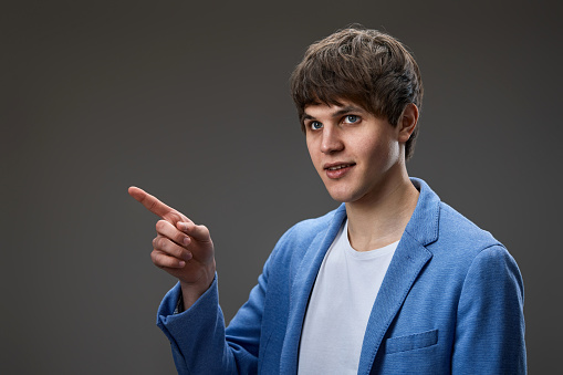 handsome caucasian young man in jacket pointing finger at empty space on gray background