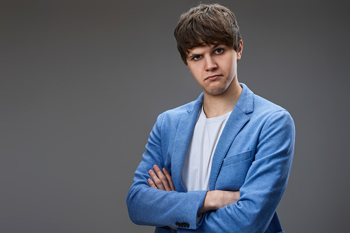 young guy in jacket posing with crossed arms and looking at the camera on gray studio background