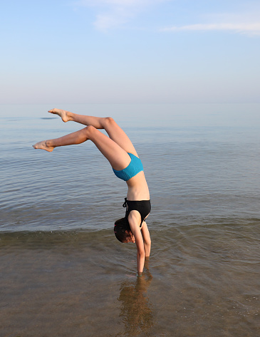 Young girl carries out gymnastic heads with her head down the sea near the coast