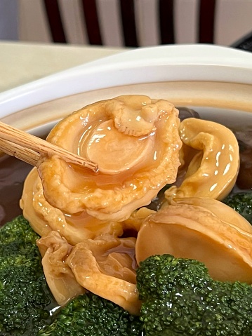 Close-up of chopstick holding a piece of cooked abalone and broccoli Chinese New Year 盆菜 dish