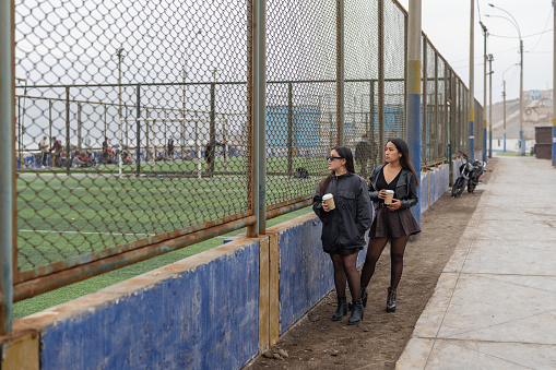 Two friends standing while having a take-away coffee in front of a football field