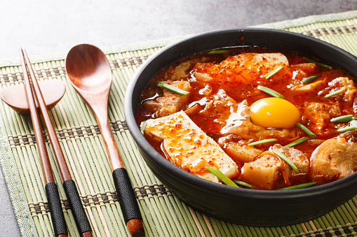 Sundubu Jjigae or soft tofu stew, is a traditional Korean dish made with silky soft uncurdled tofu coated in a spicy and flavorful broth closeup on the bowl on the table. Horizontal