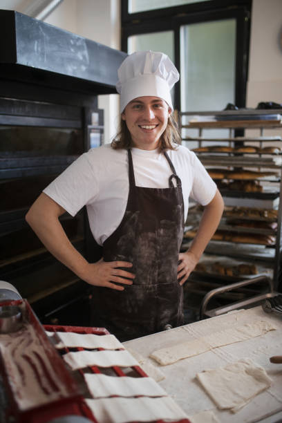 istock Young baker with chef cap preparing pastries in bakery. 1458173241