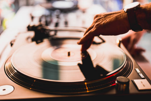 istock Dj hands on equipment deck and mixer with vinyl record at party, human hands using two vinyl turn table players playing songs in succession. 1458174898