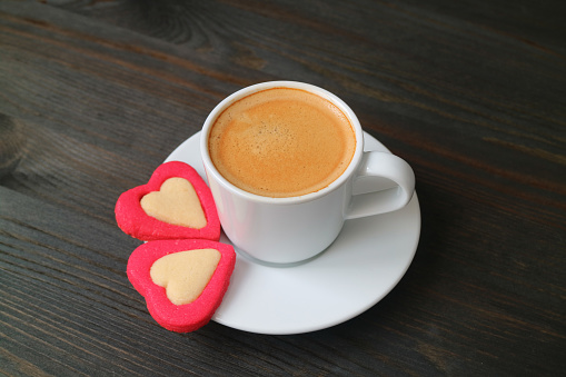 Cup of espresso coffee with a pair of heart shaped cookies on black wooden background