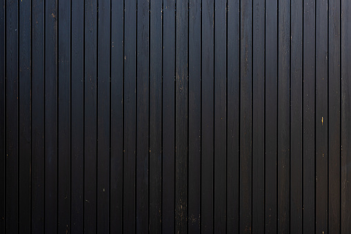 A fragment of a wooden fence made of vertical boards painted with black paint. Copy space.