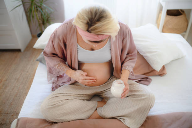 Pregnant woman creaming her belly, taking care of herself. Pregnant woman creaming her belly,sitting in a bed, taking care of herself. creaming stock pictures, royalty-free photos & images