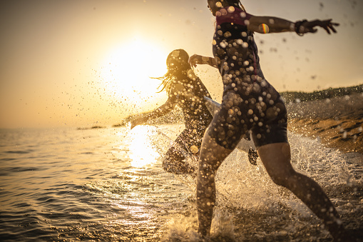 Photo of female surfers running into the water at sunset with surfboards .