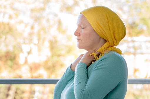 Young woman from behind putting a yellow scarf on her head because she has cancer and worried