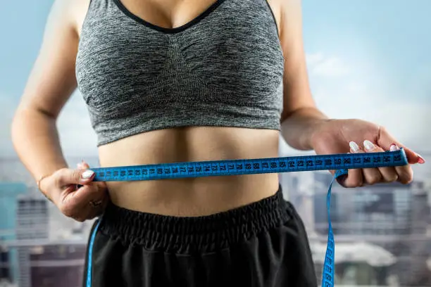 Photo of smiling woman measures her ideal waist with a tape measure and shows the result of her diet.