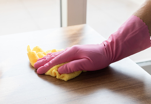 a hand in a pink glove wipes the surface with yellow microfiber.