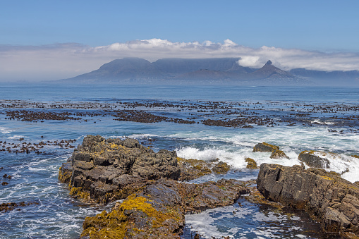 Rocky beach on a small island south of Cape Town with a distant view to the Table Mountain with clouds
