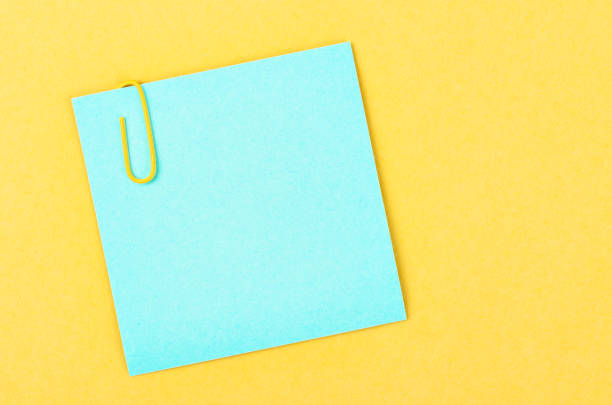 Blank blue notes paper with a paper clip on yellow background, for your text or message.