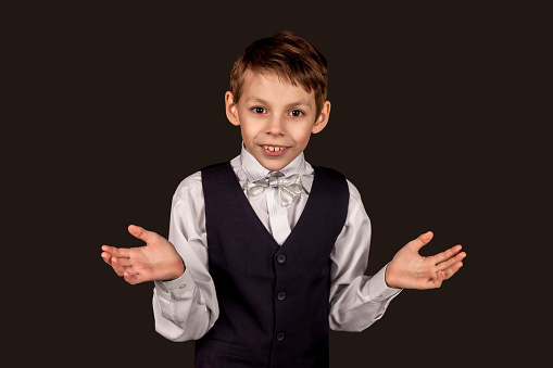 Little boy spreading his hands away wear fashionable suit with bow tie on black isolated background. Schoolboy student holding away hand from surprise in studio. Education concept. Copy text space