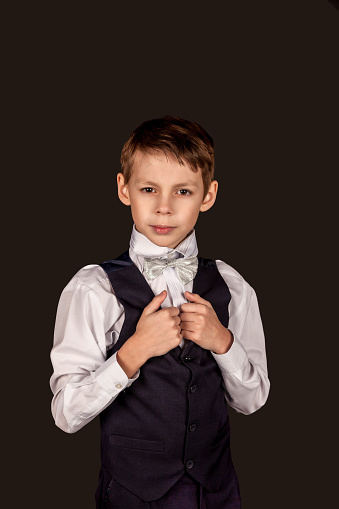 Serious schoolboy in school uniform on black isolated background. Fashionable little boy wear fashion suit with bow tie, student looking at camera in studio. Education concept. Copy text space for ad