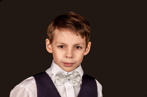 Serious face schoolboy in school uniform looking at camera on black isolated background. Stylish little boy in suit with bow tie, student posing in studio. Education concept. Copy text space for ad