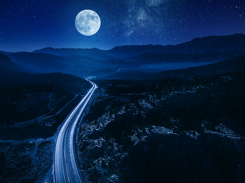 Rising moon at night over beautiful winding road in mountains. Aerial shot