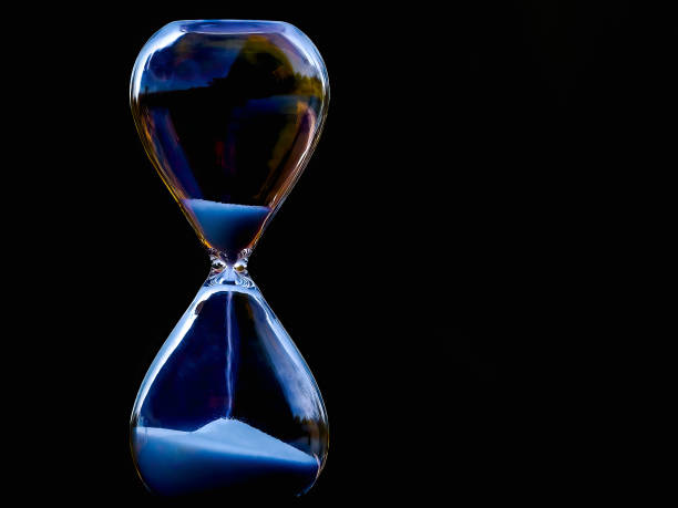 Time stands still A low-key photo depicts sand flowing through an hourglass. hourglass stock pictures, royalty-free photos & images