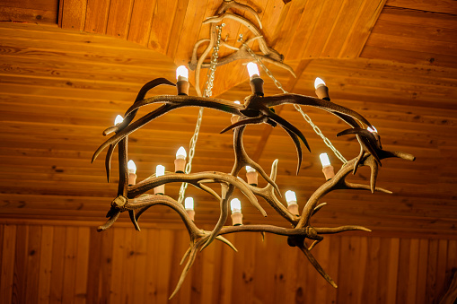 Chandelier on the ceiling made of deer antlers. A light bulb in the shape of a candle.