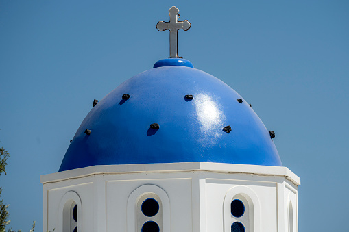 Blue and white colored Greek orthodox church, bells and cross roof, during a sunny summer day on summer in Santorini Island