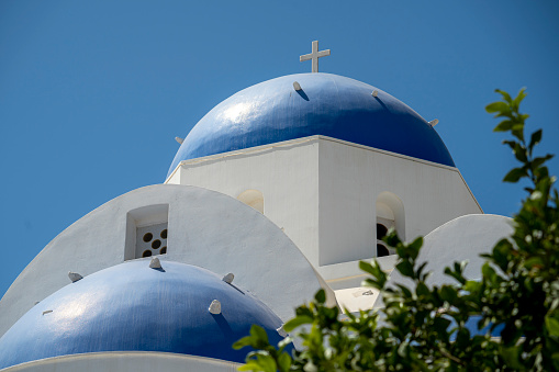 Blue and white colored Greek orthodox church, bells and cross roof, during a sunny summer day on summer in Santorini Island