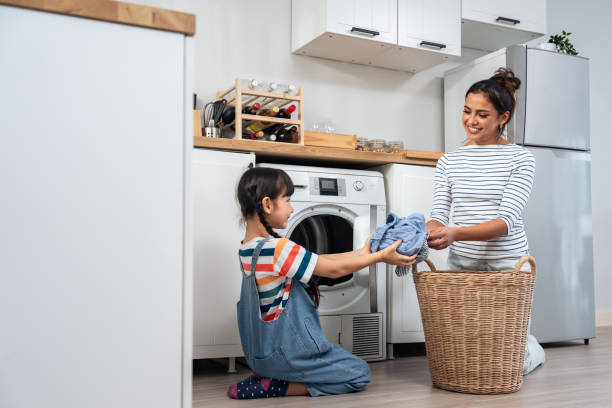 mãe caucasiana bonita ensinando filha pequena lavar roupas sujas. adorável menina menina bonita ajuda e aprender com a mãe dos pais para colocar a roupa no aparelho de lavar em casa. doméstica-housekeeping. - stereotypical housewife little girls family domestic kitchen - fotografias e filmes do acervo