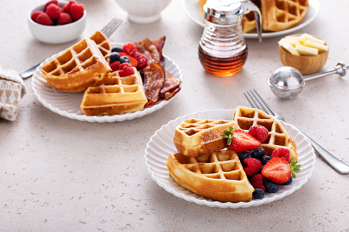 Breakfast table with waffles, berries and bacon served with maple syrup and whipped cream