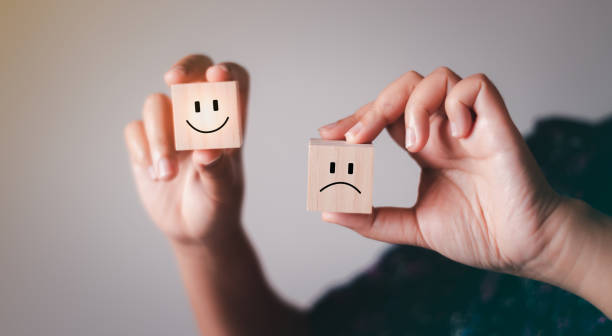 Hand showing mental health and emotional state concept, Smile face on bright side and sad face in dark side on wooden block cube for positive mindset selection. stock photo