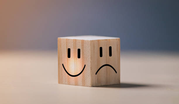 Smile face on bright side and sad face on dark side on wooden block cube for positive mindset selection. Mental health and emotional state concept. stock photo