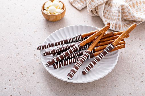 Chocolate covered pretzel rods homemade on a white plate with dark and white chocolate