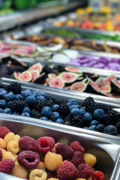 Assortment of fresh yellow raspberries, red raspberries, blueberries, blackberries, and sliced figs at a fruit bar. Shot vertically.