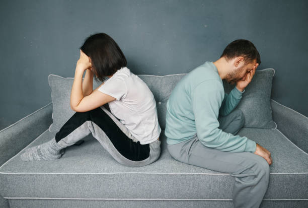 istock Young couple sitting back to back on the couch and looking offended while having a quarrel 1458233736