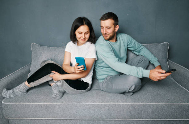 istock Young couple relaxing on sofa using mobile smart phone relaxing at home 1458233740