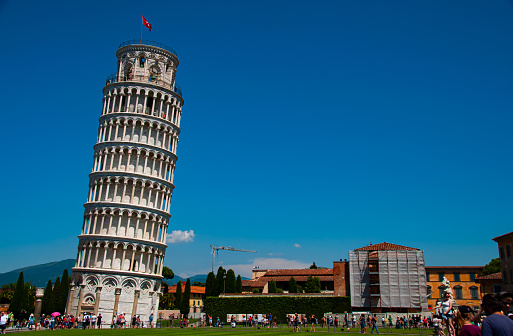 The Leaning Tower of Pisa with a grass lawn on a sunny day in the summer. Tourist crowd below with a clear blue sky in the city of Pisa