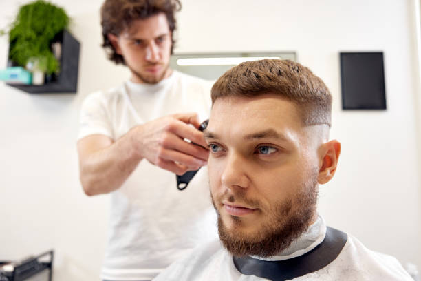istock Barber trim hair with clipper on handsome bearded man 1458234488