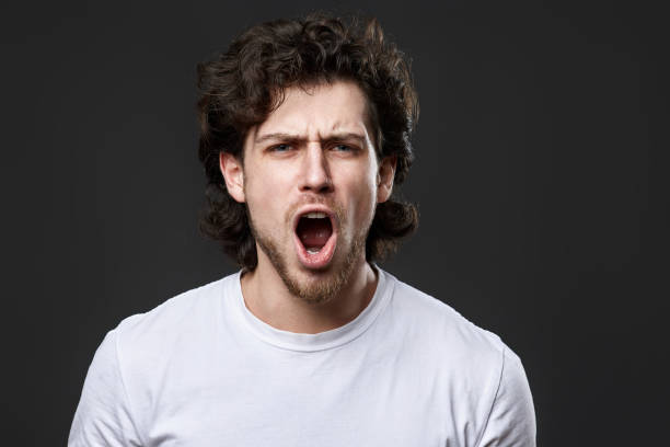 istock annoyed angry curly bearded man on dark gray studio background 1458237386