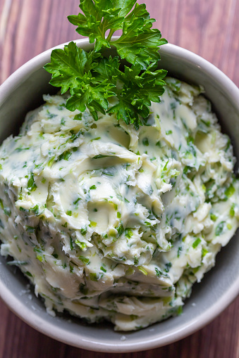Homemade spicy herb butter in a ceramic bowl, close-up, vertical, top view