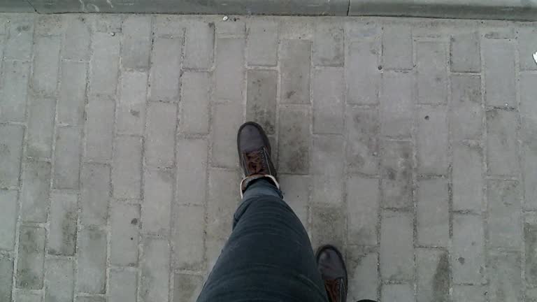 Woman legs in gray pants and brown winter boots walk along the sidewalk - top view. Video 9 seconds