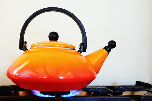 Orange kettle on a gas stove top.