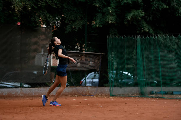 vista lateral de una jugadora de tenis activa con una raqueta de tenis en la mano detrás de la espalda - athlete flying tennis recreational pursuit fotografías e imágenes de stock