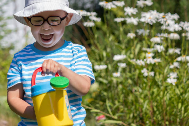 Happy kid with toy watering can plays in the garden stock photo