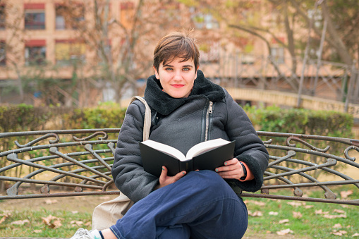 Woman with short hair looking at camera and smiling with a book in her hands