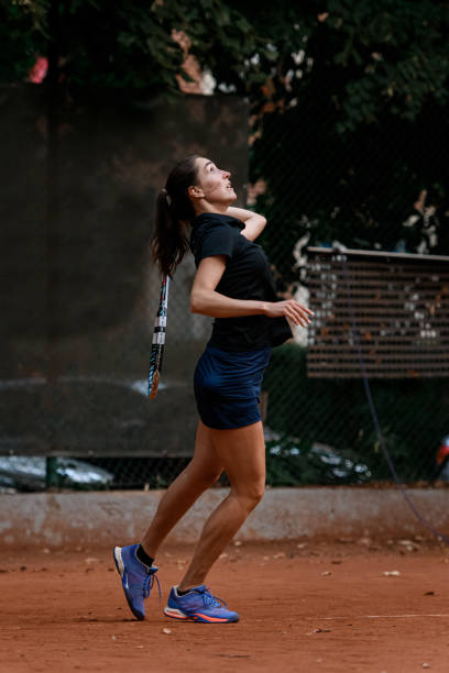 vista lateral de una jugadora de tenis deportiva con raqueta de tenis en la mano detrás de la espalda - athlete flying tennis recreational pursuit fotografías e imágenes de stock