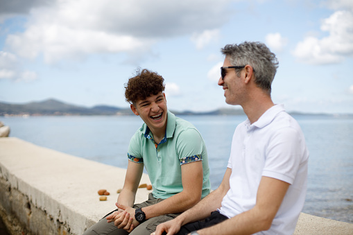 Father and son sitting on a rocky beach and talking