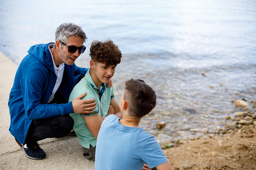 Father and sons sitting on a rocky beach and talking