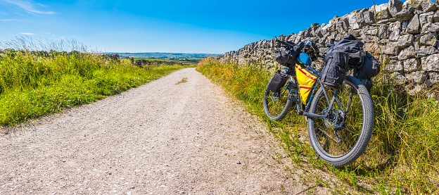 Bikepacking mountain bike with bags leaning against dry stone wall on a rough country lane in the Peak District National Park, England, UK.