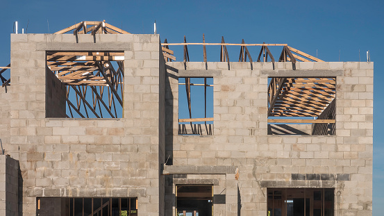 Rectangular openings for future windows below roof trusses of a two-story single-family house under construction in a suburban development on a sunny morning in southwest Florida