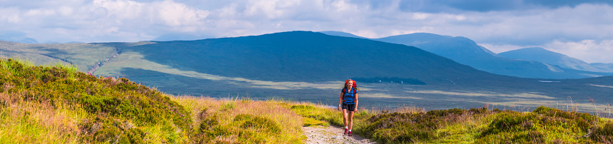 Young woman hiker walking the West Highland Way trail below the mountains of Scotland.