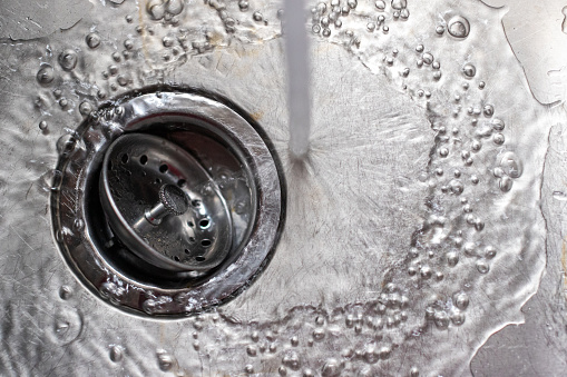 Water splashing into a steel kitchen sink and running down the drain.