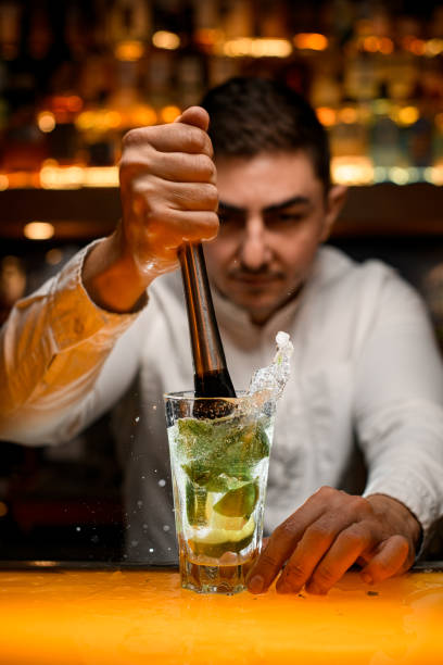 istock Bartender prepares cocktail mojito using the madler. Glass with mint and lime and ice 1458268608